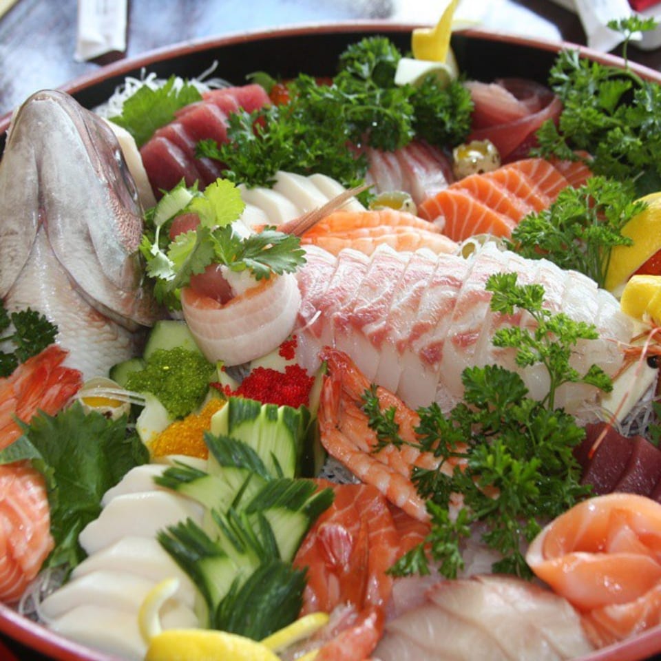 A large platter of Kanpai Izakaya sushi and sashimi, including a fish head, shrimp, and various fish slices.