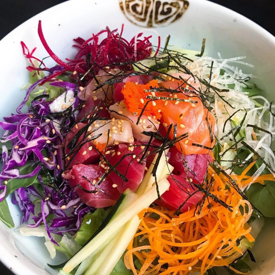 Colorful Kanpai Izakaya sushi bowl with tuna, salmon, roe, seaweed, and various shredded vegetables.