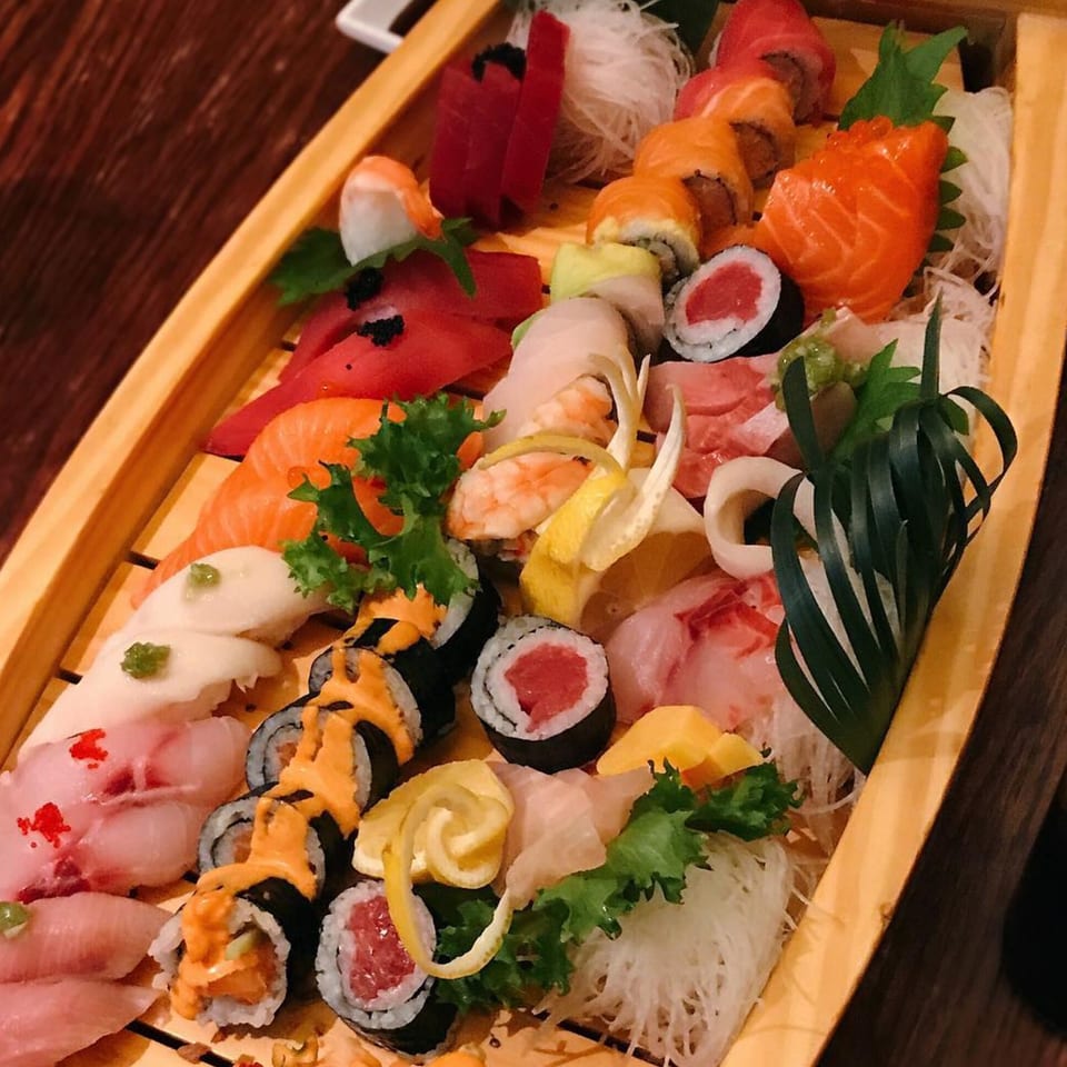 A large wooden boat filled with various sushi, sashimi, and rolls, garnished with lemon and greens.
