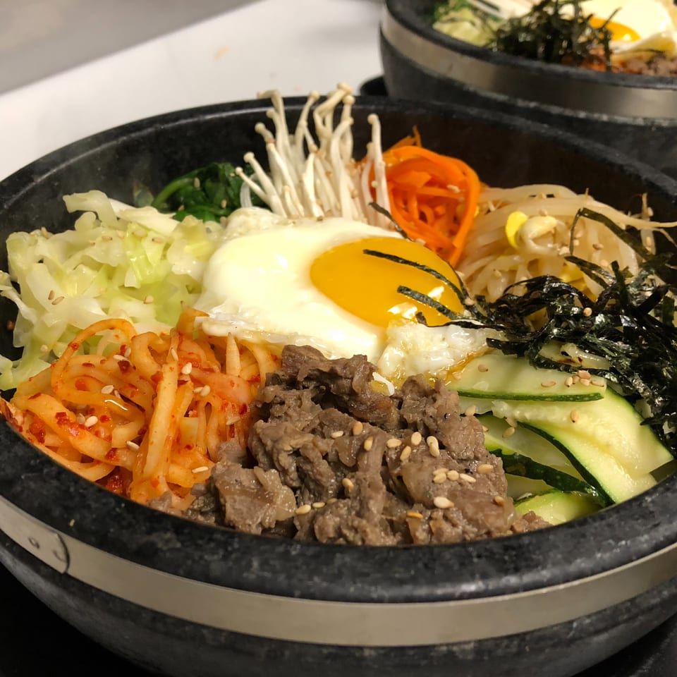 Close-up of a Kanpai Izakaya bibimbap bowl with beef, egg, vegetables, and kimchi.